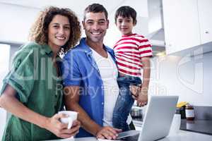 Parents using laptop with son in kitchen