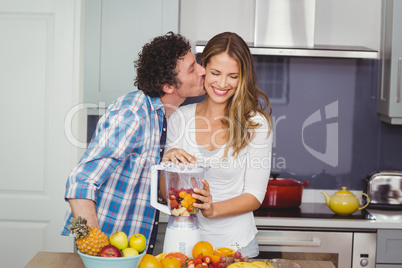 Man kissing woman preparing fruit juice