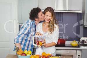 Man kissing woman preparing fruit juice