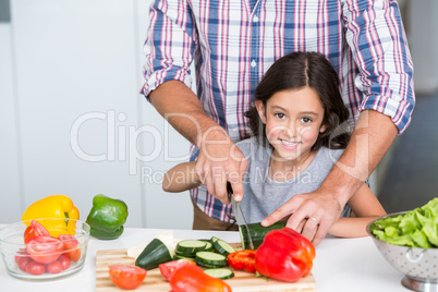 Portrait of cute daughter cutting vegetables with father