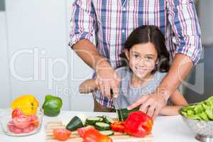 Portrait of cute daughter cutting vegetables with father