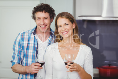 Portrait of young couple holding wineglasses in kitchen