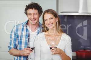 Portrait of young couple holding wineglasses in kitchen