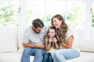 Cheerful parents with daughter on sofa