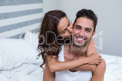 Wife kissing and embracing husband on bed