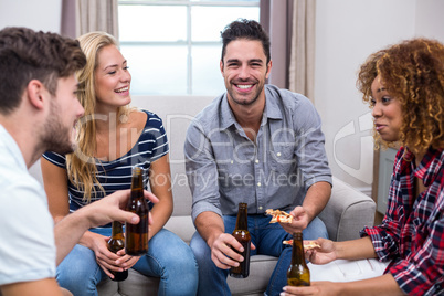 Young friends enjoying beer and pizza on sofa at home