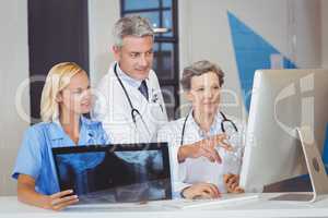 Doctor team with X-ray while discussing at computer desk
