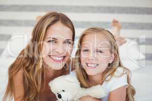 Portrait of smiling mother and daughter on bed at home