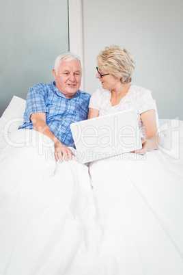 Senior couple with laptop on bed