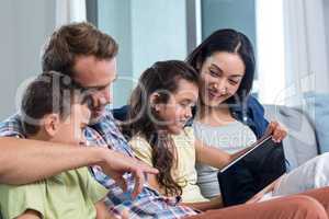 Parents sitting with son and daughter and looking at digital tab