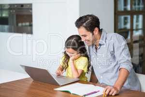 Smiling daughter working on laptop with father