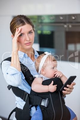 Tensed woman with mobile phone carrying baby girl