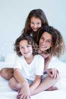 Portrait of mother and children sitting together on bed