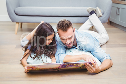 Father and daughter looking in picture book while lying on floor