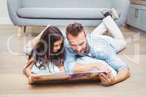 Father and daughter looking in picture book while lying on floor