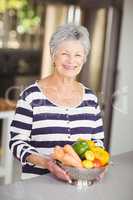 Portrait of cheerful senior woman holding colander with vegetabl