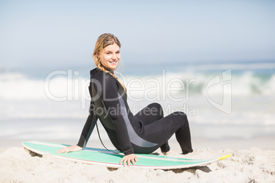 Portrait of woman in wetsuit sitting with surfboard on the beach