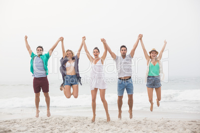 Portrait of friends holding hands and jumping on the beach