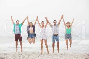 Portrait of friends holding hands and jumping on the beach