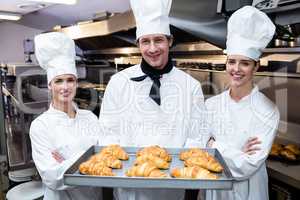 Three chefs holding a tray of baked croissant