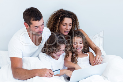 Family with credit card shopping online on bed