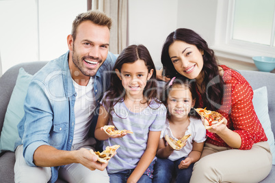 Happy family eating pizza while sitting on sofa