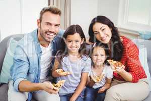 Happy family eating pizza while sitting on sofa