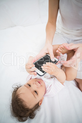 Midsection of mother holding mobile phone while playing with bab