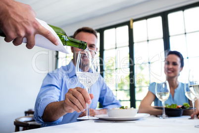 Waiter serving wine to group of friends while having lunch