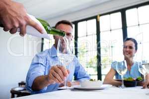 Waiter serving wine to group of friends while having lunch