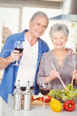Portrait of senior woman preparing salad while man standing with