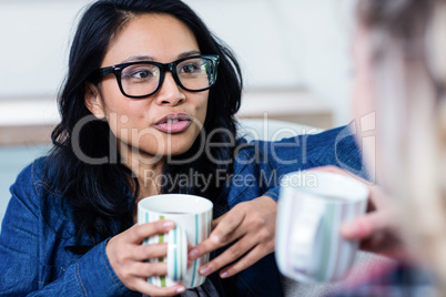 Woman talking with female friend while drinking coffee at home