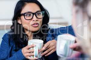 Woman talking with female friend while drinking coffee at home