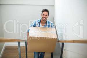 Portrait of smiling man holding cardboard box while climbing ste