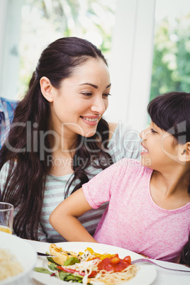 Happy mother and daughter sitting at dining table