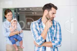Thoughtful man with wife and baby in background