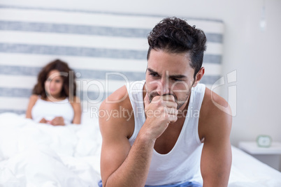 Tensed man sitting on bed while wife in background