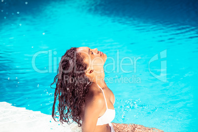 Beautiful woman in white bikini sitting by pool side