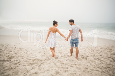 Rear view of couple holding hands and walking on the beach