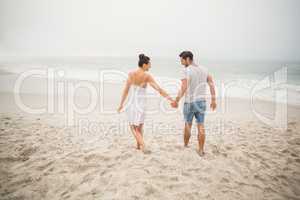 Rear view of couple holding hands and walking on the beach