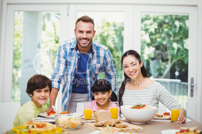 Portrait of cheerful family with father standing at dining table