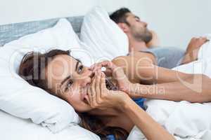 Woman talking phone on bed with husband in background