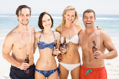Happy friends standing on the beach with beer bottles