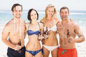 Happy friends standing on the beach with beer bottles