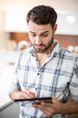 Confused young man using digital tablet in kitchen