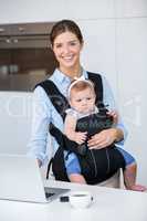 Happy woman carrying baby girl while using laptop