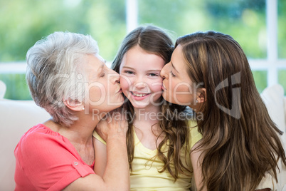 Mother and grandmother kissing happy girl on sofa