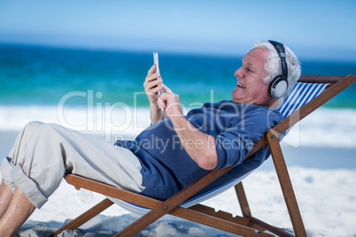 Mature man resting on a deck chair listening to music with smart
