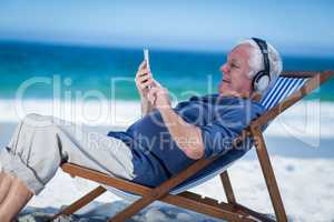 Mature man resting on a deck chair listening to music with smart
