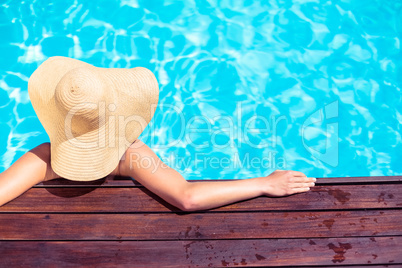 Woman wearing straw hat leaning on wooden deck by poolside